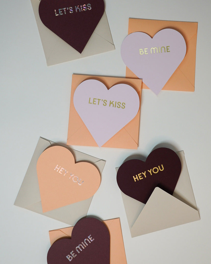 Letterpress Valentine pink and orange greeting cards in the shape of hearts with foiled lettering saying Let's Kiss, Be Mine, and Hey You, Link