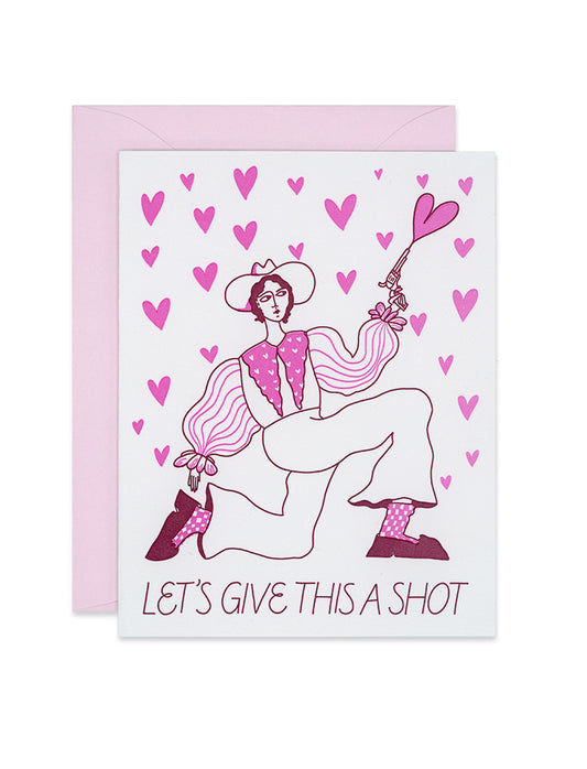 Letterpress Valentines greeting card with a woman in a cowboy hat kneeling on one leg, holding a gun that is shooting hearts